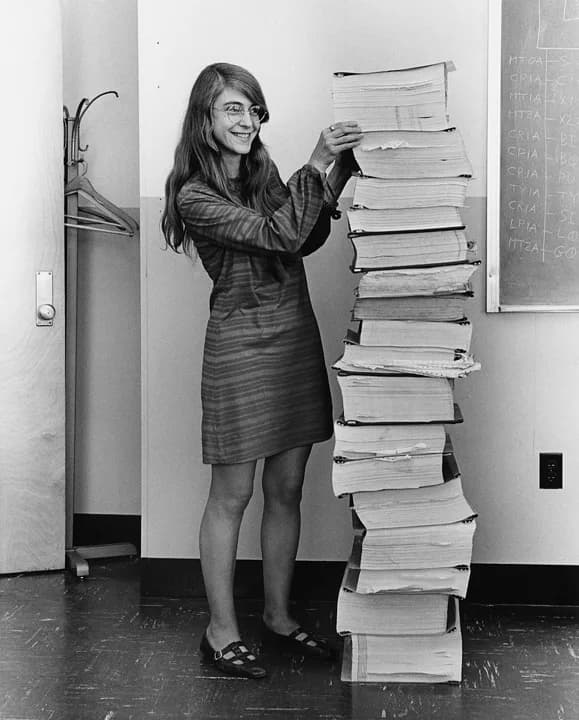 Margaret Hamilton standing beside a stack of Apollo flight-software printouts as tall as she is